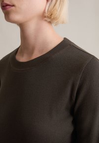 Ciemnobrązowy prążkowany sweter z okrągłym dekoltem, teksturowaną tkaniną i widocznymi szwami na kołnierzu oraz na szwach ramion.