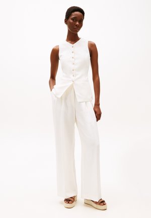 White sleeveless blouse with a button front, paired with wide-leg white trousers. The fabric appears smooth and tailored for a clean look.
