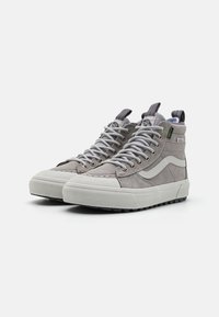Zapatillas de caña alta hechas de ante gris claro con suelas de goma blanca, paneles laterales texturizados y cordones grises. Presentan una cinta de agarre en el talón.