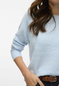 Hele sinine kootud sviiter keeratud varrukatega, pehme tekstuur, ümar kaelus, kantud tumedate teksade ja pruuni vöösid. Keskenduge ülakehale.