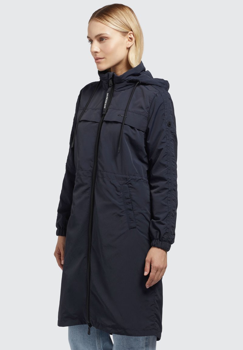 Marineblauer langer Mantel aus leichtem Material mit durchgehendem Reißverschluss, verstellbarem Kapuzenrand, Kordelzug in der Taille und elastischen Bündchen. Mit Seitentaschen ausgestattet.