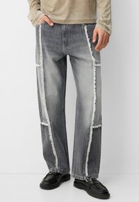 Šedé džíny z denimu s ohrnutými bočními panely, volným střihem a rovným střihem nohavic. Mají otvory na kapsy a opotřebované okraje s kontrastním prošíváním.