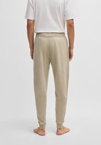 Beige joggingbroeken gemaakt van zachte stof met een elastische tailleband, afgewerkte enkels en een losse pasvorm, gezien van achteren.