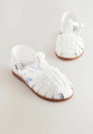 Sandalias de tiras trenzadas blancas con cierre de hebilla, con una plantilla de estampado floral y suela de goma marrón. Diseño de punta abierta.