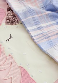 Bomuldsstof med et enhornedesign, der har detaljer i pink og fersken, palietter og et rutig overlay i pastelfarver blå og pink. Blød tekstur.