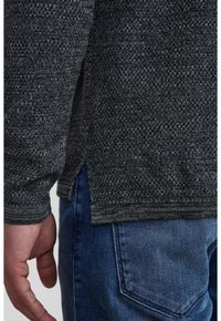 Mörkgrå, texturerad tröja med långa ärmar, med ribbade mudd och fåll, i kombination med blå denimjeans. Sidoklipp detalj synlig.