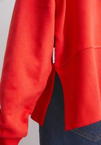 Rode sweatshirt met een geribbelde zoom, een gladde textuur en zijsplitten; inclusief een label met het merk aan de linkerkant.