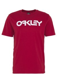 Czerwona bawełniana koszulka z okrągłym dekoltem, z dużym białym logo "OAKLEY" na przodzie. Krótkie rękawy i luźny krój.