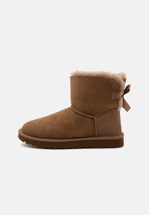 Brauner Wildleder-Stiefeletten mit weichem Fellfutter und griffiger Sohle, mit einer kleinen Schleife hinten als dekoratives Detail.