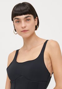 Svart ermeløs bodysuit med firkantet hals, glatt tekstur og strukturerte paneldetaljer, laget for en tettsittende silhuett.