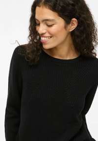 Maglione nero lavorato a maglia con un motivo a coste testurizzato e colletto rotondo. Il tessuto ha un aspetto morbido e caldo.