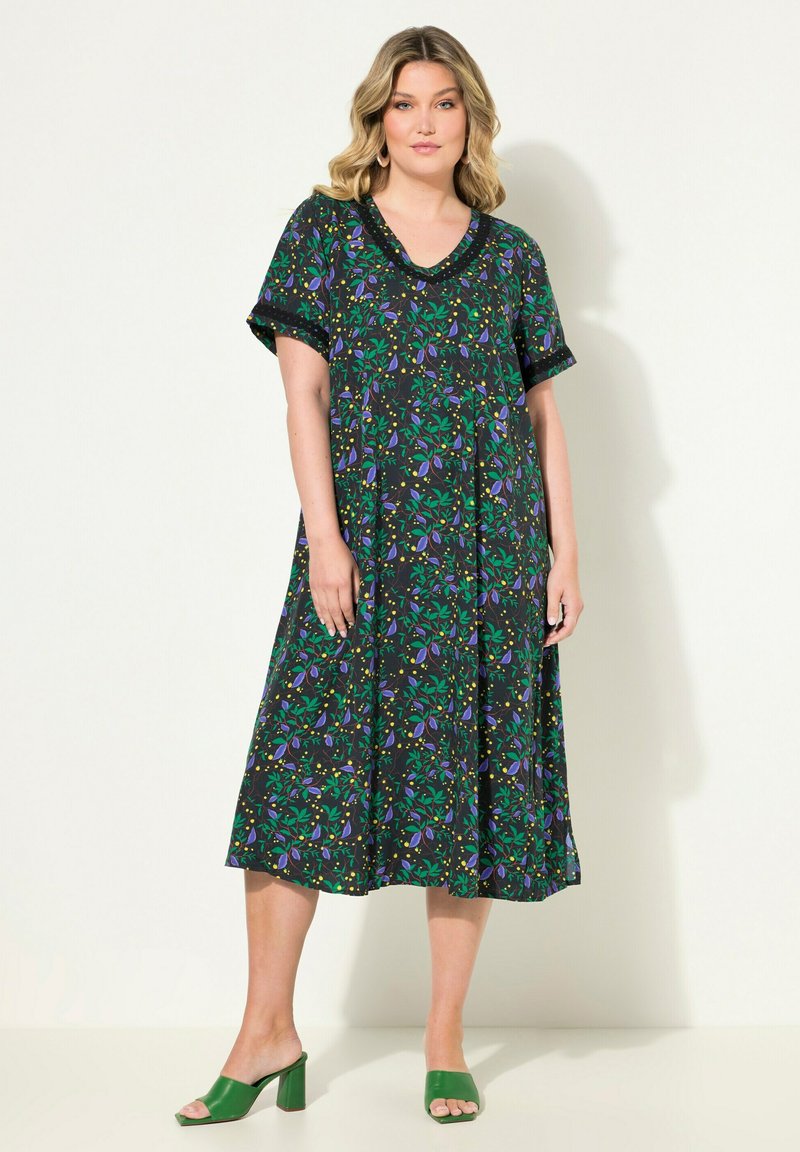 Robe à imprimé floral noire avec des motifs verts, violets et jaunes. Coupe ample, manches courtes et décolleté en V. Assortie à des sandales à talons carrés vertes.