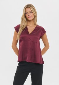 Burgundy satin topp med V-ringning, korta ärmveck och en svävande A-linjeform. Slät textur med en söm detalj över bysten.