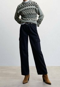 Zielony i szary sweter z dzianiny w geometryczny wzór; czarne spodnie cargo z bocznymi kieszeniami; brązowe botki na obcasie za kostkę.