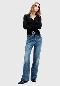 Top negro de manga larga acanalado con escote en V y tres botones, combinado con unos vaqueros de pierna ancha de denim azul claro con un lavado desgastado y costuras prominentes.