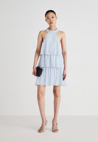 Lyseblå lagdelt kjole lavet af chiffon, med en halterneck-design og en kort, flydende kant. Sammen med sølvfarvede højhælede sandaler.