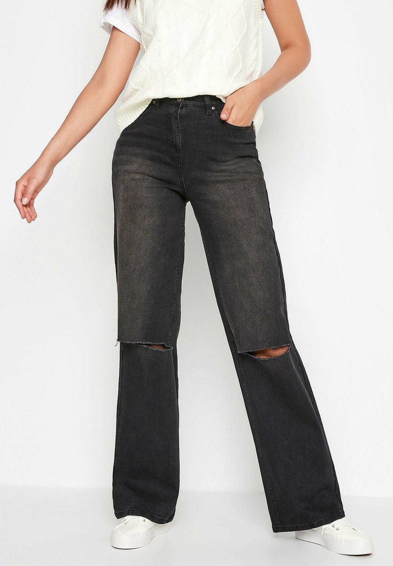 Sort brede jeans i slidseret denim med to huller ved knæene. Parret med en cremefarvet kabelstrikket sweater og hvide sneakers.