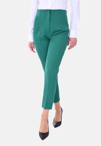 Pantaloni verdi a vita alta con una texture liscia, caratterizzati da dettagli delle cuciture e un taglio slim-fit, abbinati a tacchi a punta neri.