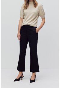 Hellbeiges Strickoberteil mit kurzen Puffärmeln, kombiniert mit schwarzen weiten Hosen, ergänzt durch schwarze Slingback-Absätze.