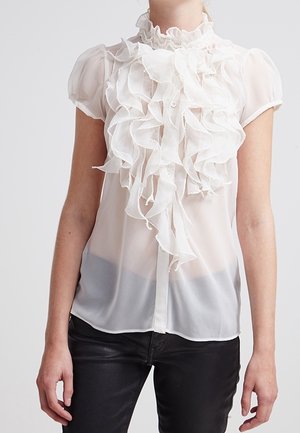 Biała bluzka z krótkim rękawem z falbaniastym detalem z przodu i wysokim dekoltem, wykonana z przezroczystej, lekkiej tkaniny, połączona z ciemnymi spodniami o slim fit.