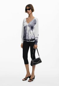 Top bianco a maniche lunghe con stampa floreale grigia e testo; leggings neri; borsa nera con cuciture arricchite; sandali neri con cinturini.
