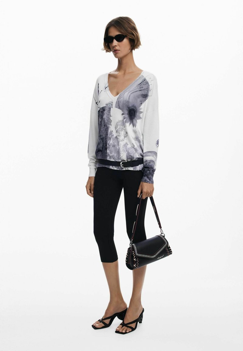 Top bianco a maniche lunghe con stampa floreale grigia e testo; leggings neri; borsa nera con cuciture arricchite; sandali neri con cinturini.