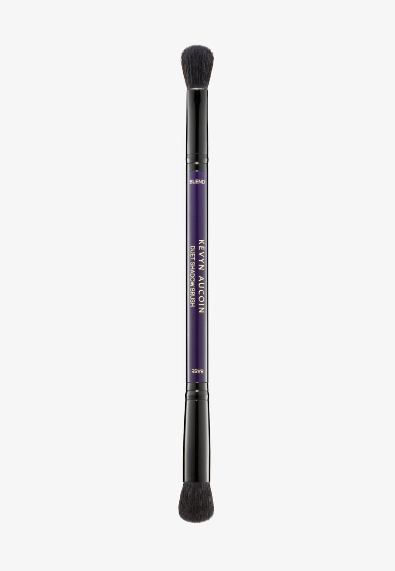 Dual-ended eyeshadow brush with black bristles, a tapered and rounded shape, purple handle, and gold text labeling. Smooth texture.