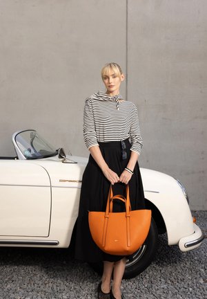 Orange textured handbag with dual handles, worn with a black skirt and striped top. Vintage white convertible visible in background.