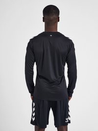 Zwarte sportshirt met lange mouwen en ronde hals, zachte stof. Gecombineerd met zwarte shorts met een wit chevronpatroon.