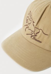 Beige bomullcaps med en buet skygge som har et brunt brodert hestedesign og merke tekst. Strukturert stoff med synlige sømdetaljer.