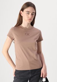 Ruda medvilnė marškinėliai su trumpomis rankovėmis, apvalia iškirpte ir įsiūtu "CK" logotipu ant krūtinės. Lygus paviršius, prigludusi forma.