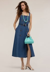 Robe en denim avec décolleté carré, boutons et fente latérale. Comprend une ceinture avec une boucle ronde. Associée à un sac à main turquoise et un collier en perles.