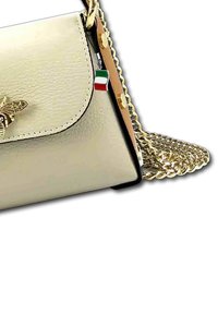 Sac à main en cuir doré avec un rabat, un emblème décoratif d'abeille et une bandoulière en chaîne dorée. Comprend un petit charme représentant le drapeau italien.