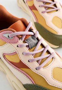 Mångfärgad sneaker som kännetecknas av en kombination av mesh- och mockamaterial. Framträdande nyanser inkluderar rosa, orange, gult och gröna accenter.