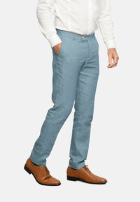 Pantalones de lino azul claro con corte recto, que cuentan con bolsillos frontales y un cierre de botón simple, combinados con zapatos de vestir de cuero marrón.