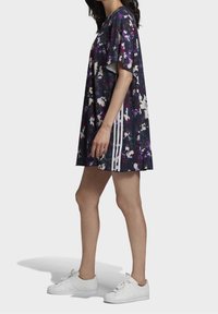 Šaty s krátkým rukávem v tmavém květinovém vzoru s bílými akcenty a třemi vertikálními pruhy po straně, vyrobené z lehkého materiálu.