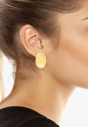 Gule harpiks ovale ørepiercinger båret på en models øre, med en glat overflade, semi-uforståelig finish og en let reflekterende tekstur.