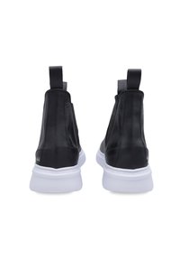 Zapatillas negras de caña alta hechas de cuero suave con suela de goma blanca. Presentan lengüetas en la parte trasera y un branding mínimo.