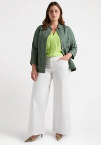Giacca verde button-up su un top verde brillante, abbinata a pantaloni bianchi a gamba larga e tacchi in stampa serpente. Tessuto morbido e vestibilità su misura.