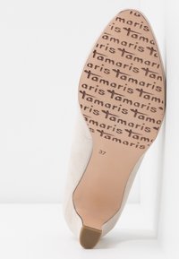Semelle de chaussure beige à bout pointu avec le nom de marque « tamaris » en relief de manière répétée pour l'adhérence, pointure 37 indiquée près du talon.
