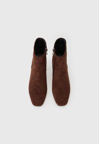 Bottines en daim marron avec un bout pointu, dotées d'une fermeture éclair sur le côté et d'une doublure noire lisse. Design simple, sans motifs visibles.