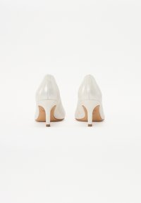 White leather high heels with a shiny finish, pointed toe, and a slim stiletto heel. Light tan insole with branding visible.
