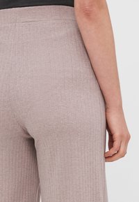 Pantalones de tela acanalada en rosa claro con cintura alta y cinturilla elástica. El detalle textural presenta líneas verticales y un acabado suave.