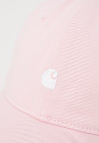 Boné de algodão rosa com uma textura canelada, apresentando um logótipo bordado branco de um lado. Visíveis costuras na aba curvada.