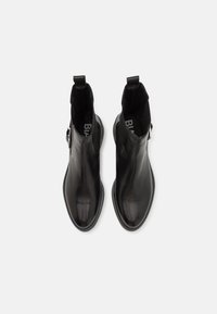 Bottines en cuir noir avec une finition lisse, des panneaux latéraux élastiques, une semelle plate et une sangle décorative avec une boucle en argent.