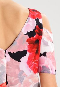 Robes florales avec un imprimé coloré de fleurs rouges et roses sur un fond clair, à manches courtes et avec un zip dans le dos.