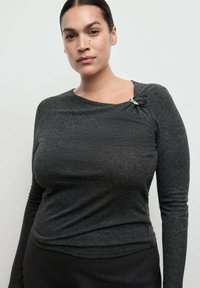 Bluză cu mâneci lungi de culoare gri închis, cu un detaliu legat la umăr și un accent argintiu. Textură moale și siluetă ajustată.