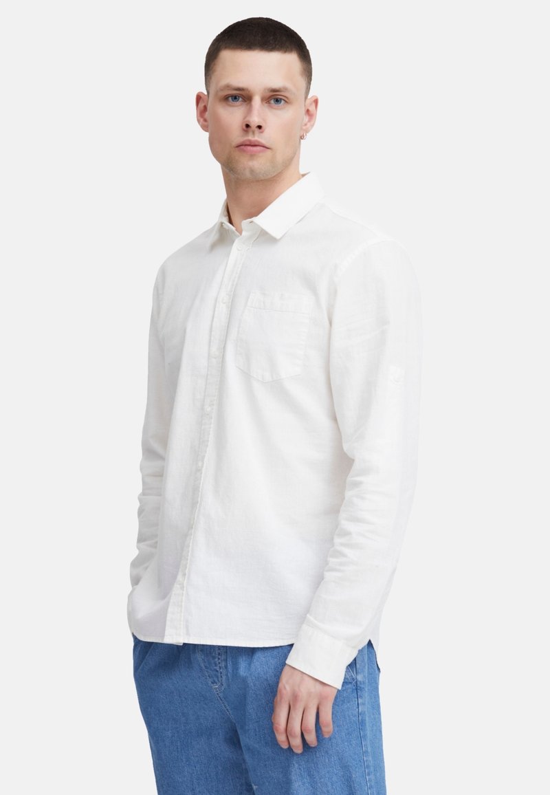 Weißes Langarmhemd aus leichtem Stoff mit Button-Down-Kragen, einer einzelnen Brusttasche und eher lockerer Passform, kombiniert mit blauen Jeans.