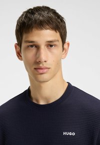 Maglione blu navy con un design in maglia waffle testurizzata. Presenta un collo a giro e un piccolo logo bianco "HUGO" sul petto.