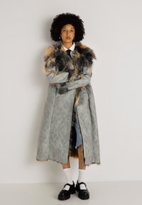 Garšs pelēks mētelis ar rakstainu tekstūru un pūkainu, daudzkrāsainu apkakli; valkāts virs džinsa svārkiem un apvienots ar baltām zeķēm un melniem apaviem.